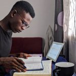 Young man deeply immersed in reading and studying with books and tablet.