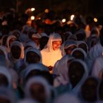 Young girl participates in Ethiopian Orthodox candlelight vigil, surrounded by worshippers in traditional attire.