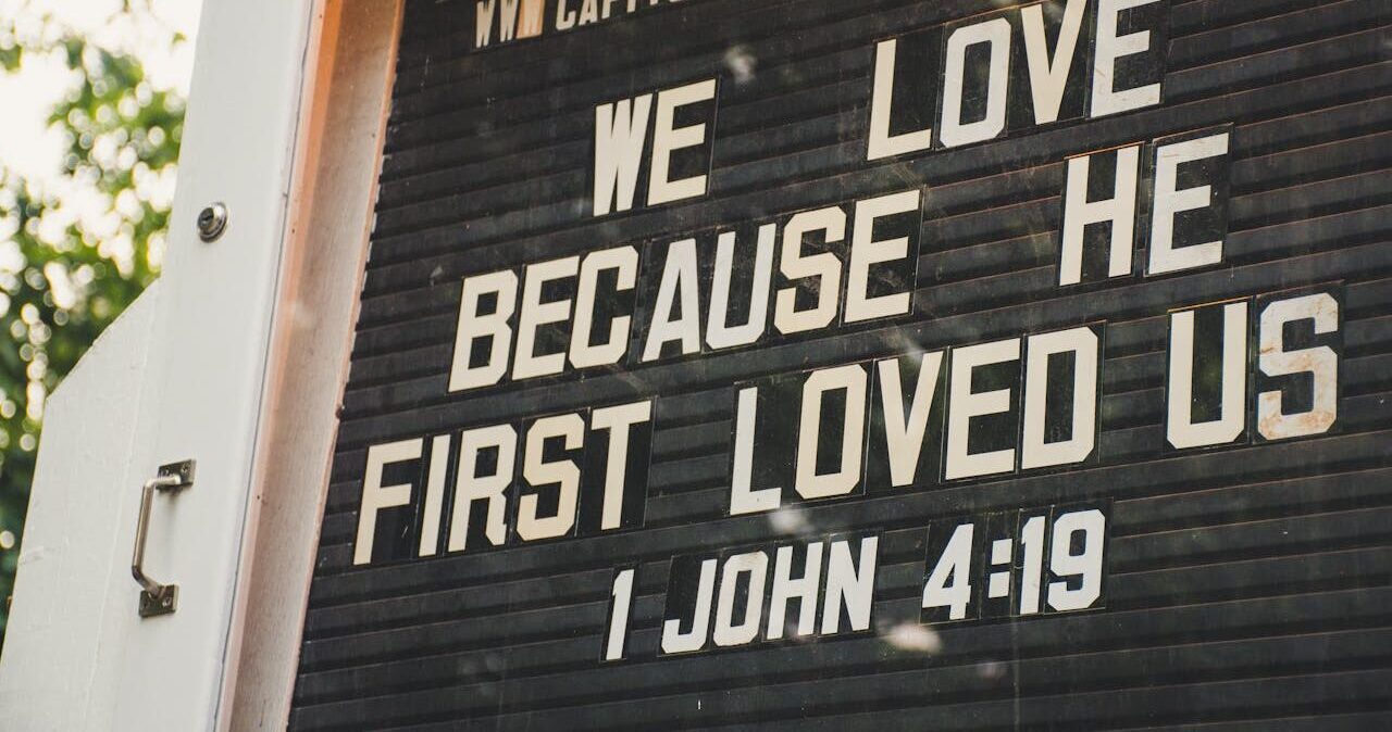 Church sign displaying biblical verse about love from 1 John 4:19 in outdoor setting.